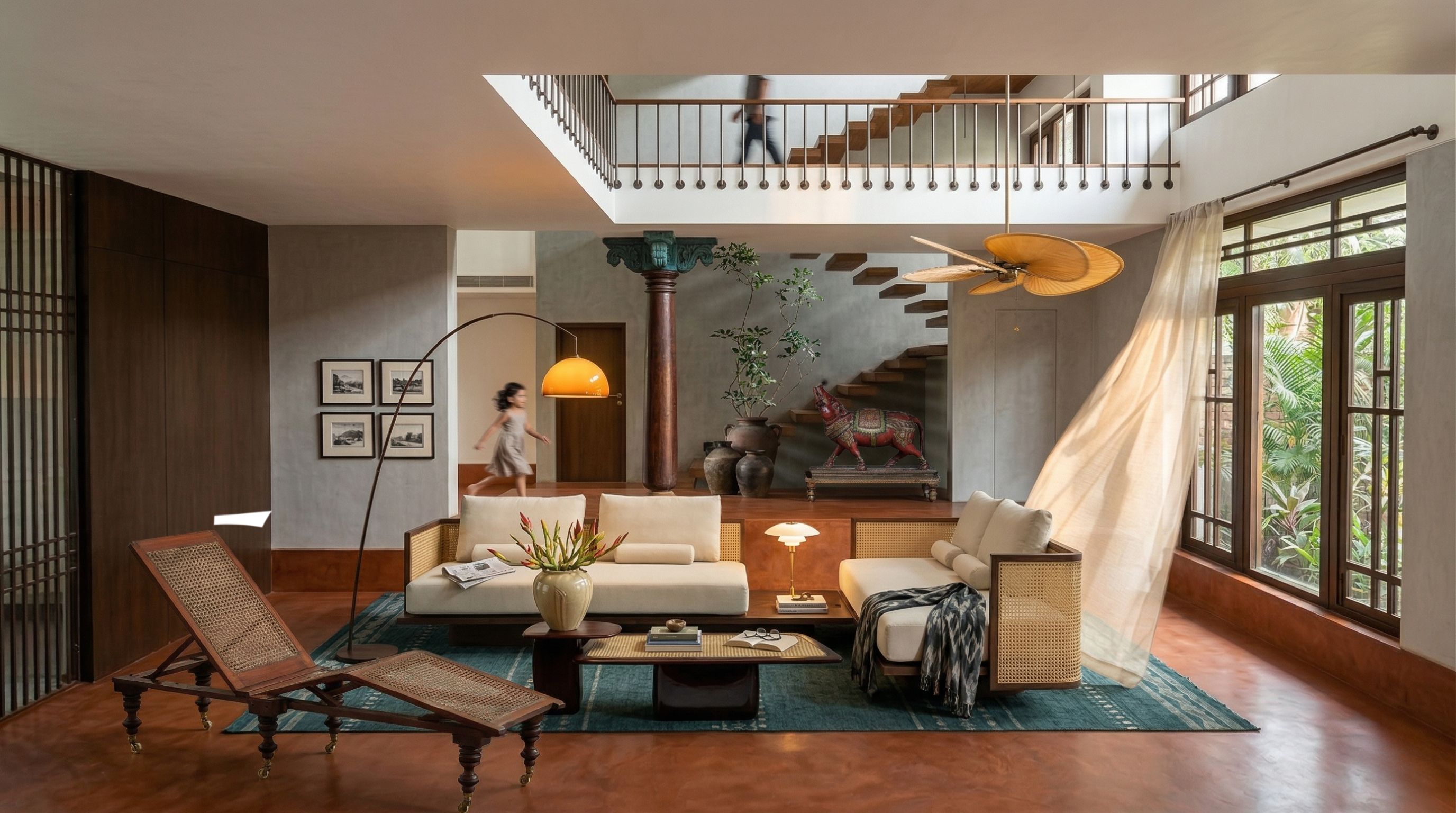 A double-height living space with a heritage column, painted bull sculpture, cane furniture, and tropical greenery